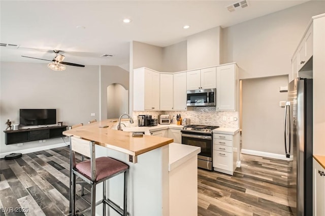 kitchen with white cabinetry, backsplash, a kitchen bar, kitchen peninsula, and stainless steel appliances