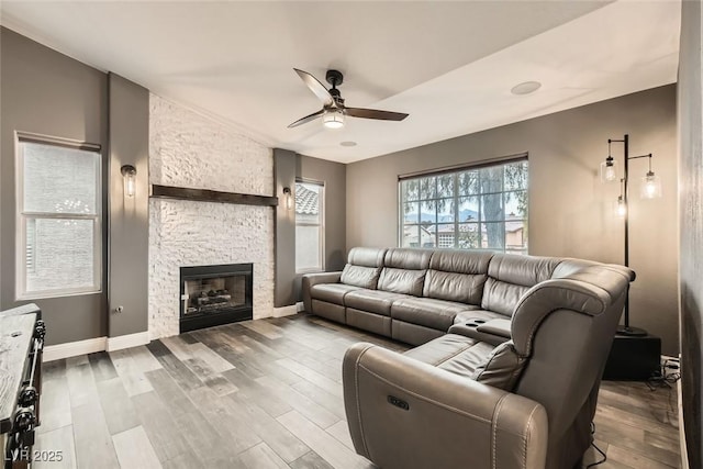 living room with a stone fireplace, wood-type flooring, and ceiling fan