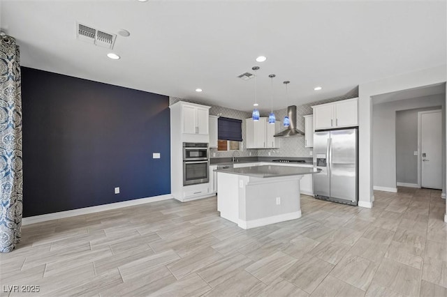 kitchen with a kitchen island, white cabinets, hanging light fixtures, stainless steel appliances, and wall chimney exhaust hood