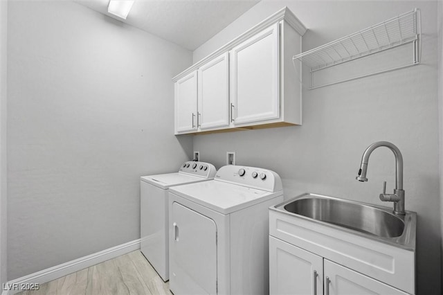 clothes washing area with sink, light hardwood / wood-style flooring, cabinets, and washing machine and clothes dryer