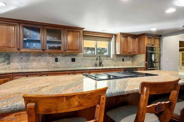 kitchen featuring sink, a breakfast bar, double oven, light stone counters, and a kitchen island