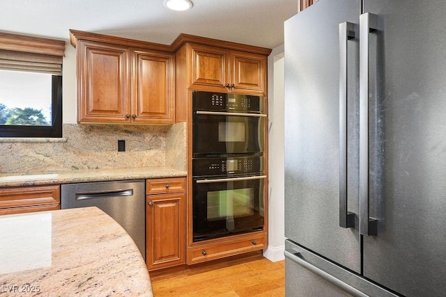 kitchen featuring stainless steel appliances, tasteful backsplash, light stone counters, and light hardwood / wood-style flooring