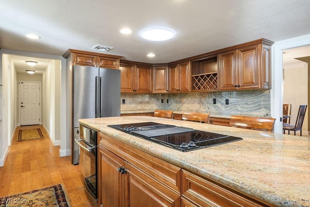 kitchen featuring light stone countertops, backsplash, black electric cooktop, and light hardwood / wood-style floors