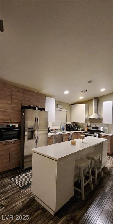 kitchen with white cabinetry, appliances with stainless steel finishes, a center island, and wall chimney range hood