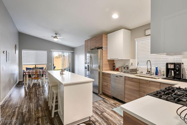 kitchen featuring vaulted ceiling, appliances with stainless steel finishes, hardwood / wood-style floors, a kitchen bar, and a center island