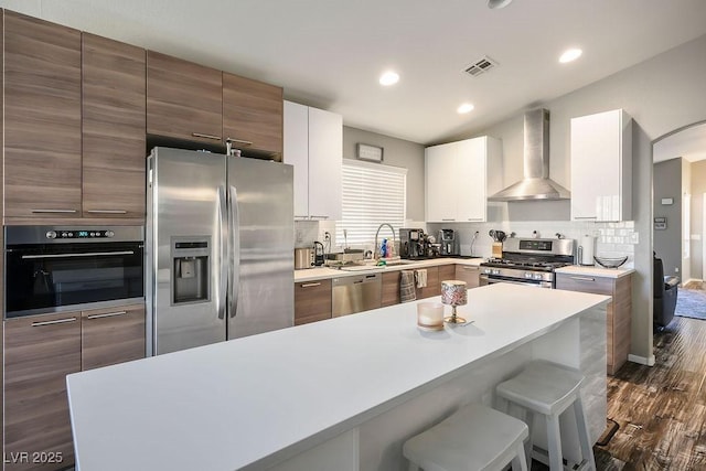 kitchen with a breakfast bar, white cabinetry, tasteful backsplash, stainless steel appliances, and wall chimney range hood