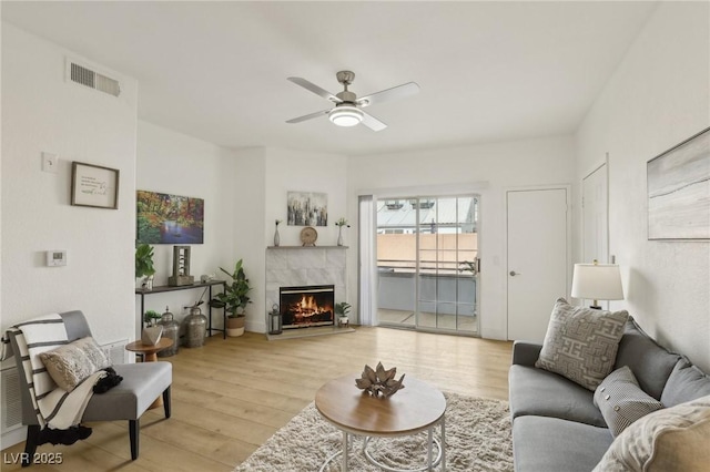 living room with ceiling fan, a fireplace, and light hardwood / wood-style flooring