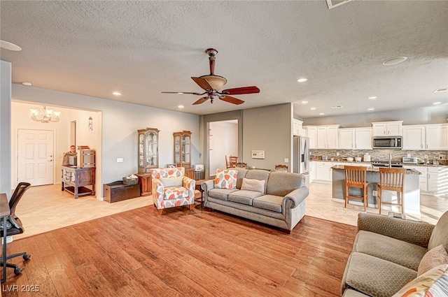 living room featuring ceiling fan with notable chandelier, a textured ceiling, and light hardwood / wood-style flooring