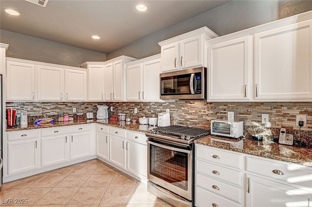 kitchen featuring white cabinetry, stainless steel appliances, backsplash, and dark stone countertops