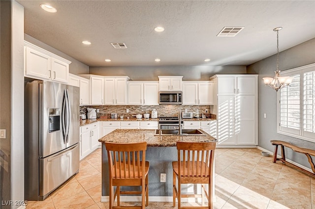 kitchen with a breakfast bar area, white cabinetry, stainless steel appliances, tasteful backsplash, and an island with sink