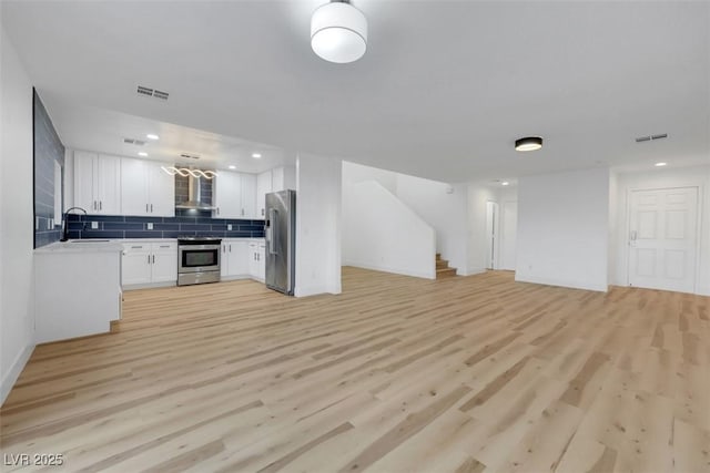 kitchen featuring appliances with stainless steel finishes, white cabinets, decorative backsplash, wall chimney range hood, and light wood-type flooring