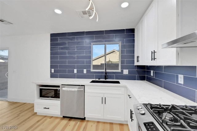 kitchen with white cabinetry, stainless steel appliances, sink, and light stone counters