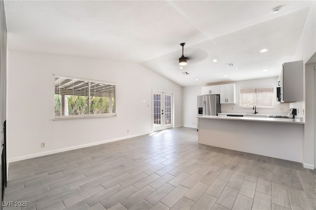 kitchen featuring french doors, stainless steel refrigerator with ice dispenser, light countertops, vaulted ceiling, and a peninsula