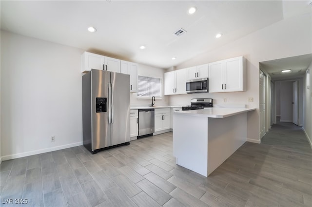 kitchen featuring white cabinets, lofted ceiling, appliances with stainless steel finishes, a peninsula, and a sink