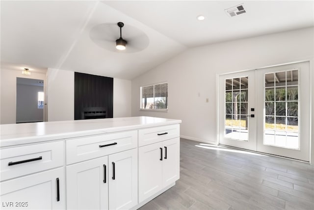 kitchen featuring a ceiling fan, visible vents, vaulted ceiling, white cabinetry, and french doors