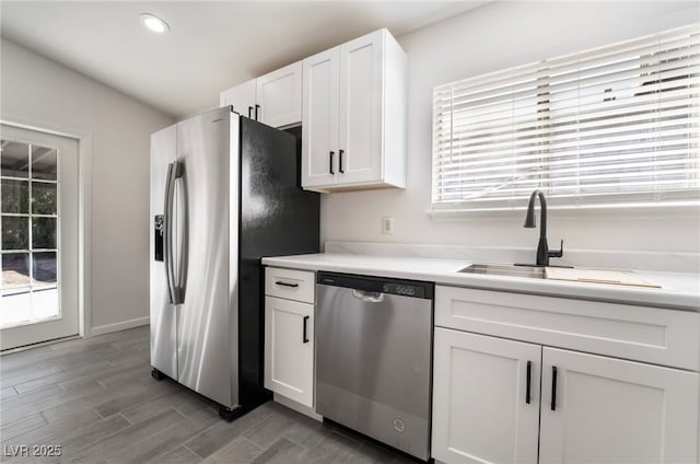 kitchen with wood finish floors, light countertops, appliances with stainless steel finishes, white cabinetry, and a sink