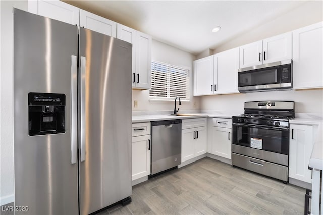 kitchen featuring white cabinetry, stainless steel appliances, a sink, and light countertops