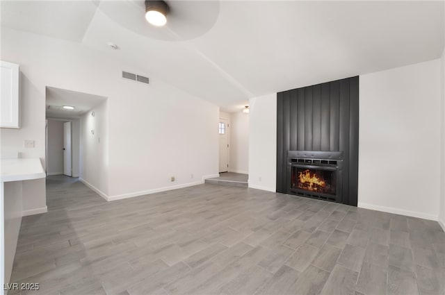 unfurnished living room with lofted ceiling, visible vents, light wood-style flooring, a large fireplace, and baseboards