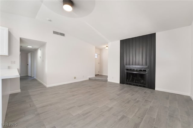 unfurnished living room with baseboards, visible vents, vaulted ceiling, and light wood finished floors