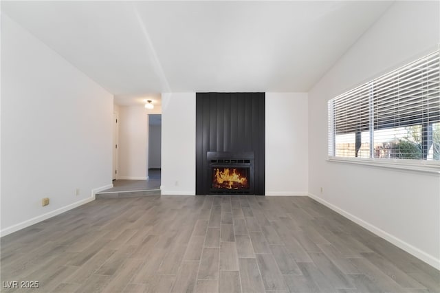 unfurnished living room featuring a fireplace, baseboards, and wood finished floors