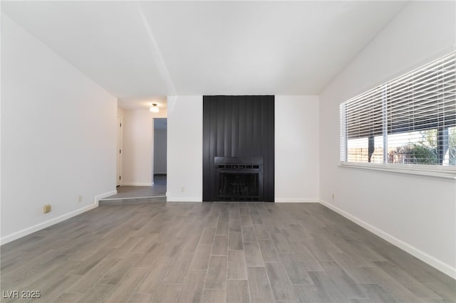 unfurnished living room featuring a fireplace, baseboards, and wood finished floors