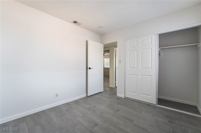 unfurnished bedroom featuring dark wood-style floors, a closet, visible vents, and baseboards