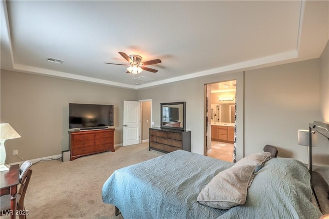 carpeted bedroom with ceiling fan, a raised ceiling, and ensuite bath