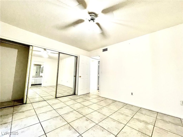 unfurnished bedroom featuring light tile patterned flooring, a textured ceiling, ceiling fan, and a closet