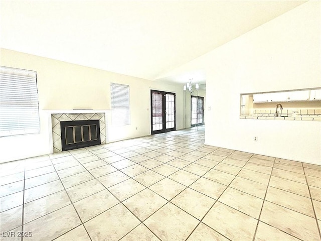 unfurnished living room with lofted ceiling, light tile patterned floors, sink, a tiled fireplace, and french doors