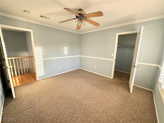 unfurnished bedroom featuring ornamental molding, carpet, a spacious closet, ceiling fan, and a closet