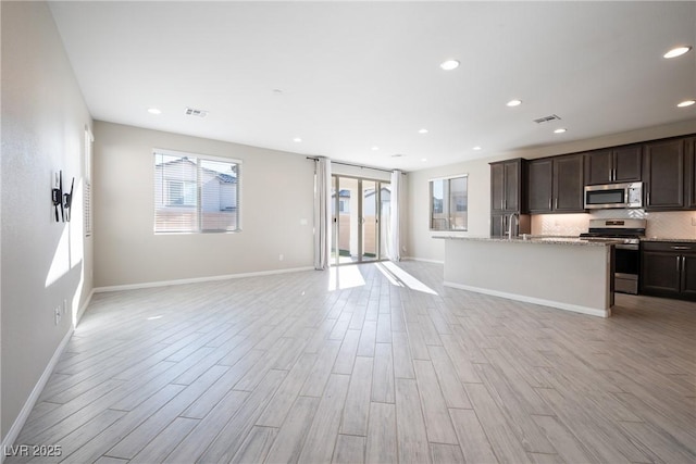 interior space with visible vents, appliances with stainless steel finishes, open floor plan, dark brown cabinets, and light wood-type flooring