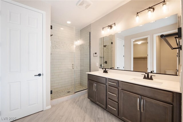 full bath featuring double vanity, a shower stall, a walk in closet, and a sink