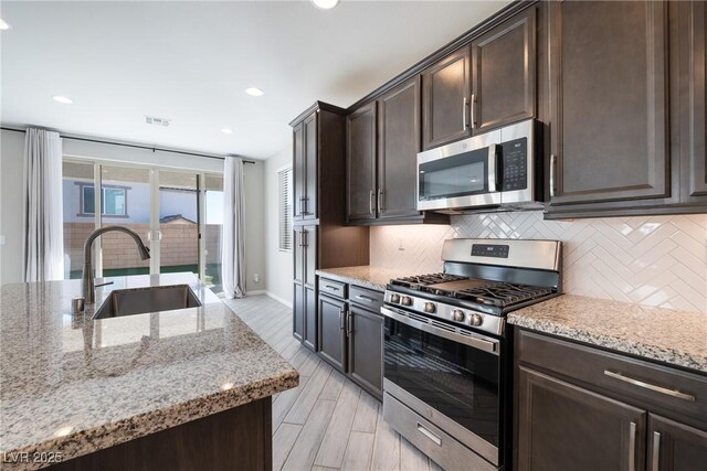 kitchen with light stone counters, sink, backsplash, and stainless steel appliances