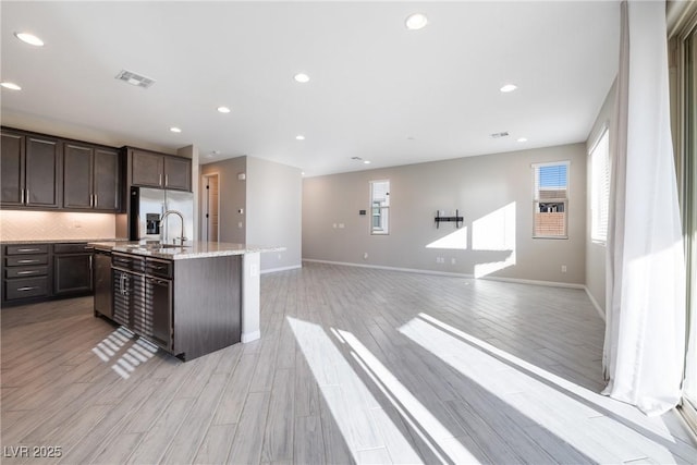 kitchen with a center island with sink, light wood finished floors, visible vents, appliances with stainless steel finishes, and dark brown cabinets