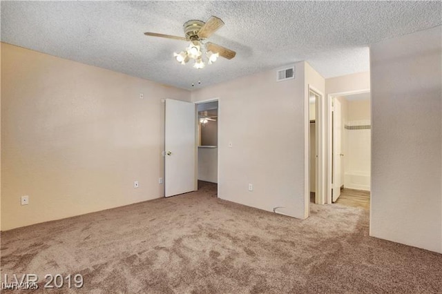 unfurnished bedroom with light carpet, ceiling fan, a spacious closet, and a textured ceiling