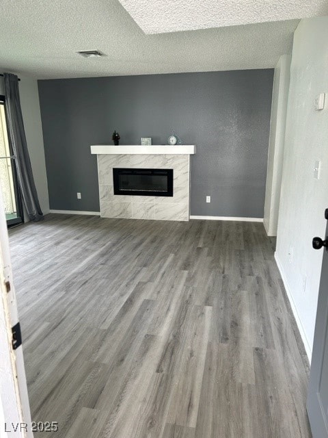 unfurnished living room featuring hardwood / wood-style flooring, a textured ceiling, and a high end fireplace