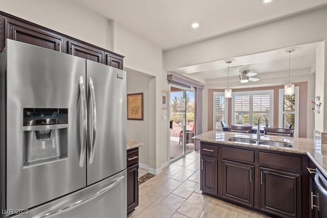 kitchen with sink, hanging light fixtures, dark brown cabinetry, light stone counters, and stainless steel fridge with ice dispenser