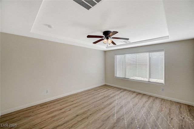 spare room featuring light hardwood / wood-style flooring, ceiling fan, and a tray ceiling