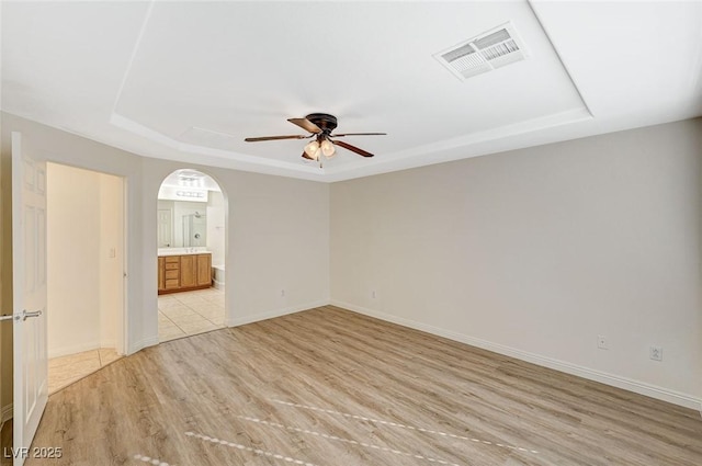 unfurnished room with ceiling fan, a tray ceiling, and light hardwood / wood-style floors