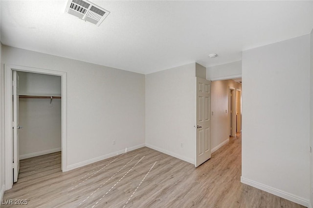 unfurnished bedroom with a walk in closet, a closet, and light wood-type flooring