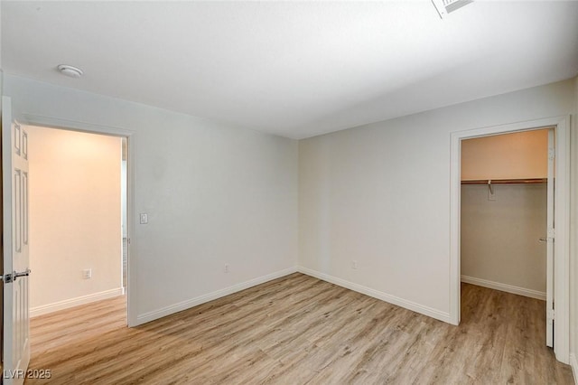 unfurnished bedroom featuring a walk in closet, light hardwood / wood-style floors, and a closet