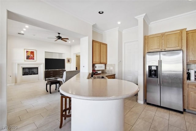 kitchen featuring stainless steel fridge, a glass covered fireplace, a breakfast bar area, a peninsula, and a sink