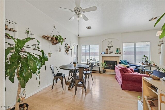 dining space with a tile fireplace, light hardwood / wood-style floors, a textured ceiling, and a wealth of natural light