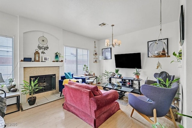 living room featuring a chandelier, light wood-style flooring, a tile fireplace, and visible vents