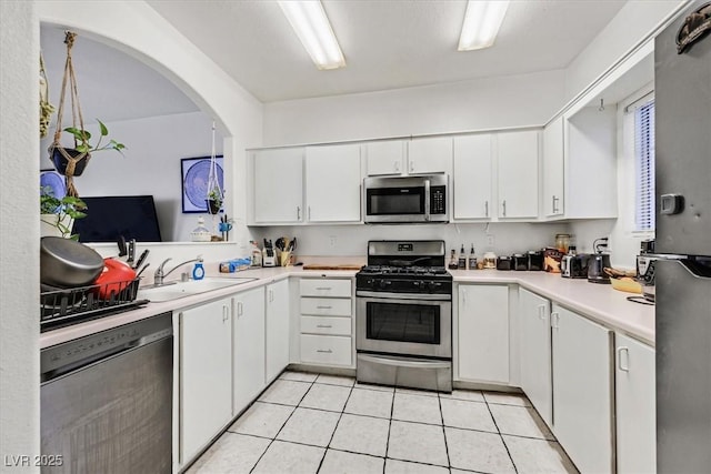 kitchen featuring light countertops, appliances with stainless steel finishes, white cabinets, a sink, and light tile patterned flooring