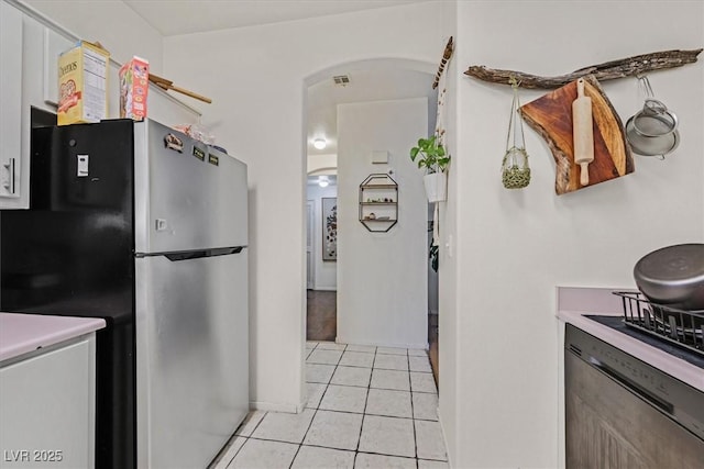 kitchen featuring arched walkways, light tile patterned floors, light countertops, visible vents, and freestanding refrigerator