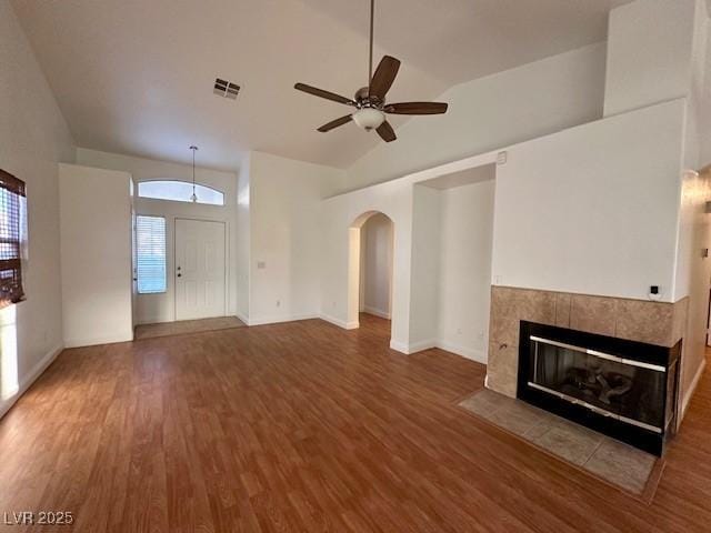 unfurnished living room featuring a tiled fireplace, wood-type flooring, lofted ceiling, and ceiling fan