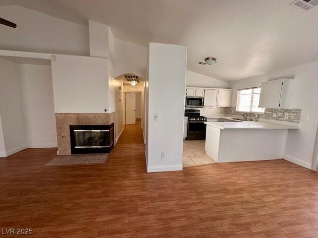 kitchen featuring white cabinetry, lofted ceiling, kitchen peninsula, gas stove, and light wood-type flooring