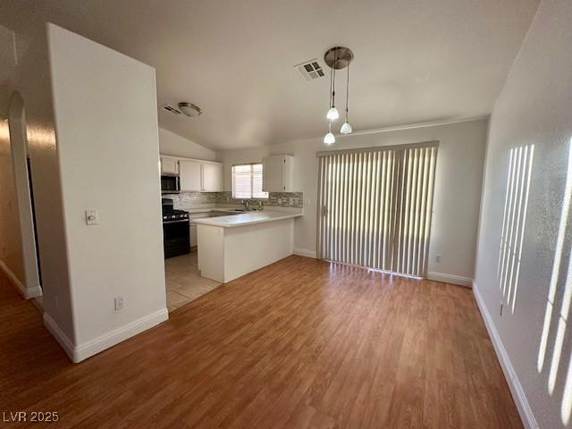 kitchen with light hardwood / wood-style flooring, white cabinetry, hanging light fixtures, range with gas cooktop, and kitchen peninsula