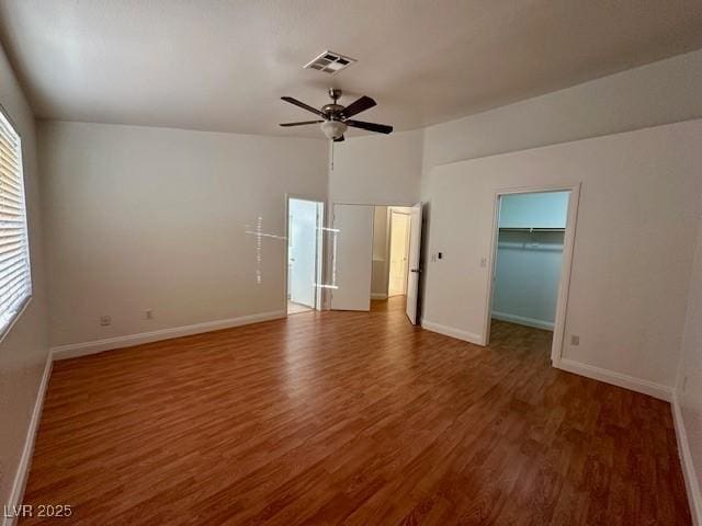 unfurnished bedroom with a closet, a walk in closet, dark hardwood / wood-style floors, and ceiling fan